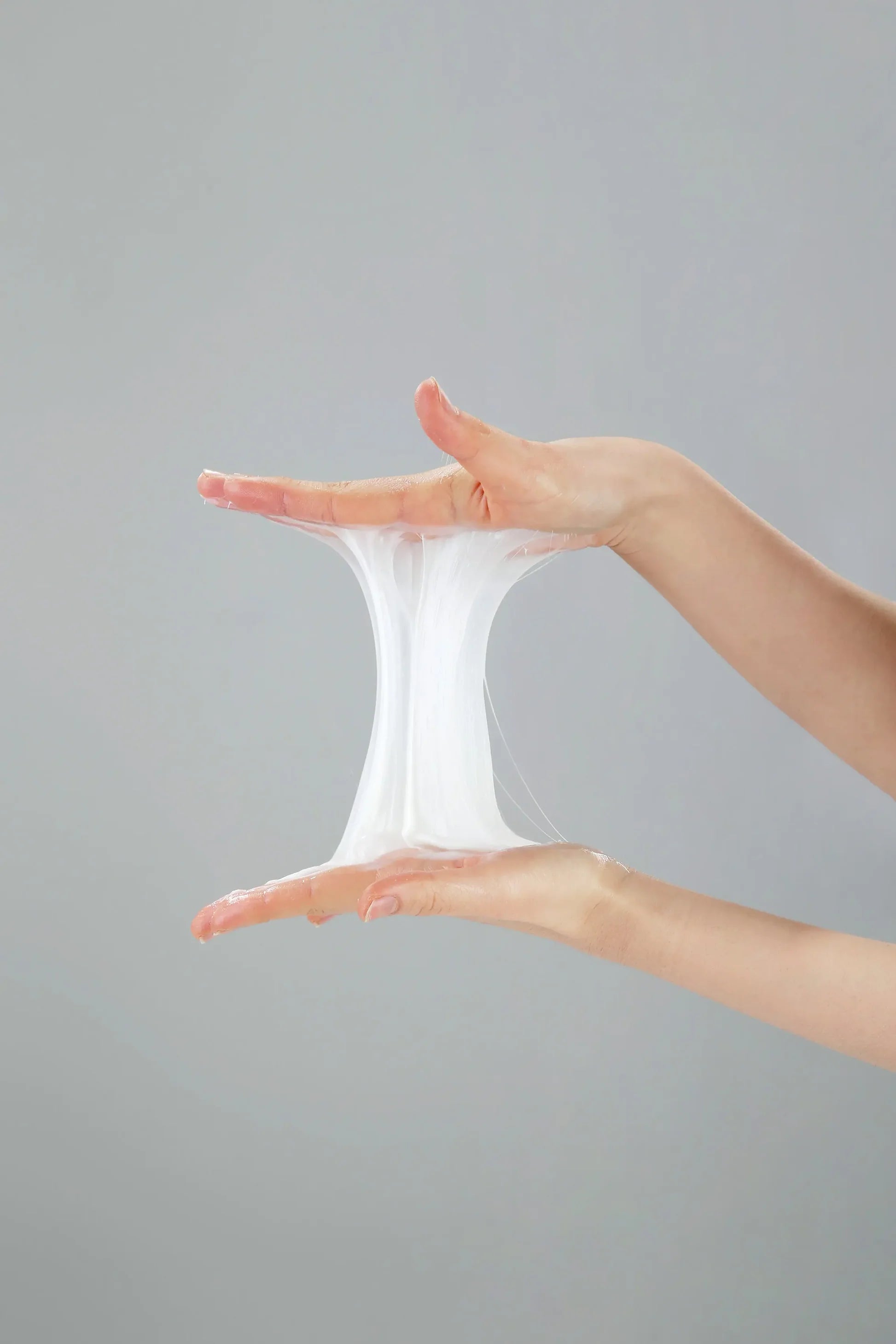 Two hands holding a small cloud of white fluffy substance against a gray background